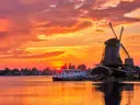 Hollandse windmolens en een boot aan het water tijdens een felrode zonsondergang.