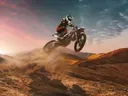 Motorcrosser die een sprong maakt boven zanderige woestijnheuvels bij zonsondergang