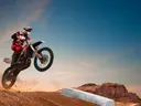 Motorcrosser maakt een sprong op een crossmotor in een woestijnlandschap.