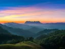 Beboste bergketens met nevel, bij zonsopkomst met een oranje en paarse lucht.