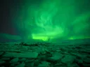 Groen noorderlicht aan de hemel boven een besneeuwde ijsvlakte.