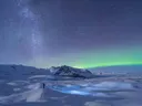 Persoon die naar de sterrenhemel met noorderlicht kijkt boven een besneeuwd gletsjerlandschap.