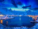 Noors dorp aan een fjord omgeven door besneeuwde bergen bij nacht met sterrenhemel.