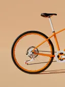 Close-up van een oranje fietswiel tegen een zandkleurige achtergrond