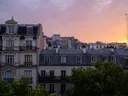 Parijse daken en gebouwen onder een roze-oranje avondlucht bij zonsondergang
