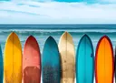 Foto van meerdere kleurrijke surfboards rechtop in het zand met de oceaan op de achtergrond