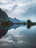 Karstbergen met spiegelend rivierwater onder een bewolkte lucht.