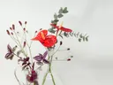 Een boeket met rode bloemen, eucalyptustakken en paarse bladeren in twee glazen vazen.