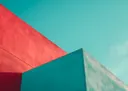 Minimalistische architectuurfoto van rode en turquoise gebouwhoeken tegen een blauwe lucht