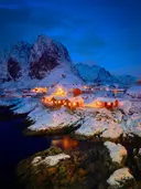 Rode vissershutten bij besneeuwde bergen aan een fjord in de schemering.