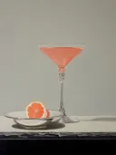 Roze cocktail in een glas naast een grapefruitpartje