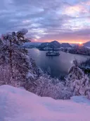 Besneeuwd bergmeer met eilandje bij zonsopkomst en roze lucht.