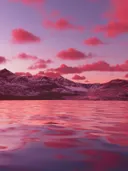 Roze zonsondergang boven een besneeuwde bergketen met een spiegelend meer op de voorgrond.