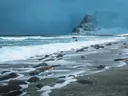 Schuimende golven op een rotsachtig strand met besneeuwde bergen op de achtergrond