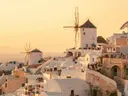 Witte huizen en een windmolen op Santorini tijdens zonsondergang, met toeristen op het terras.