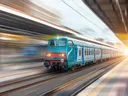 Een blauw-witte trein in beweging op een station, met wazige lichtstrepen door de snelheid.