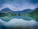 Bergmeer met perfecte spiegeling van omliggende groene bergen onder een bewolkte lucht