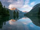 Alpenmeer met spiegelbeeld van bergtoppen en sparrenbos.