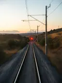 Spoorrails die in de verte samenkomen bij een rood sein, met bovenleidingen tegen een schemerige lucht.