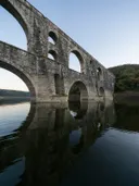 Een oude stenen aquaductbrug met meerdere rondbogen, weerspiegeld in kalm water.