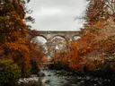 Stenen spoorviaduct tussen herfstbomen boven een rivier.