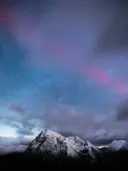 Sterrenhemel met poollicht boven een besneeuwde bergpiek in de nacht.