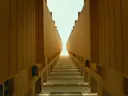 Symmetrische betonnen gevels van een modern gebouw die een smalle passage omlijsten, met zicht op de lucht.
