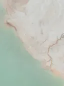 Luchtfoto van turkoois water grenzend aan een zandige kustvlakte met kleine kreekjes.