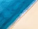 Luchtfoto van een strand met helder turquoise zee en golvende branding op wit zand.