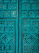 Close-up van een turquoise houten deur met metalen sierspijkers en ornamenten