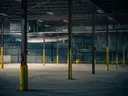 Interieur van een verlaten fabriekshal met gele pilaren.
