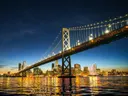De verlichte Bay Bridge in San Francisco bij nacht met de skyline van de stad en lichtreflecties in het water.