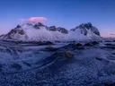 Besneeuwde bergketen boven een zwart zandstrand bij zonsopkomst.