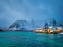 Gele vissershutten aan een fjord met besneeuwde bergen op de Lofoten in Noorwegen