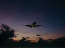Een vliegtuig landt in silhouet tegen een paarse en oranje schemerlucht met wolken.