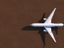 Luchtfoto van een vliegtuig van bovenaf boven een roodbruine, egale ondergrond met lange schaduw.