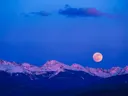 Volle maan die opkomt boven besneeuwde bergen tijdens de schemering