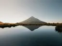 Foto van een besneeuwde berg die weerspiegelt in een rustig meer.