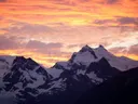 Zonsondergang met oranje wolkenlucht boven besneeuwde bergtoppen en gletsjers.