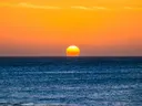 Felle oranje zon die ondergaat boven een uitgestrekte zee.