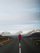 Persoon in rode jas loopt over een weg richting besneeuwde bergen.