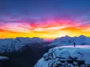 Silhouet van een wandelaar op een besneeuwde bergtop met een felgekleurde avondlucht.