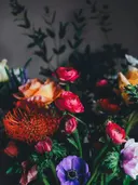 Kleurrijk bloemboeket met rozen en anemonen tegen een donkere achtergrond.