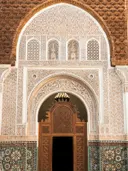 Ornate gestuukte boogingang van een religieus gebouw met houten deur en kleurrijke tegelmozaïek onderaan.