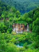 Waterval tussen groene bomen die uitmondt in een turquoise poel.