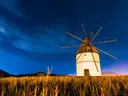 Een verlichte windmolen in een grasveld onder een sterrenhemel in de schemering.