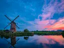 Traditionele windmolen aan het water bij zonsondergang met roze en blauwe wolkenlucht