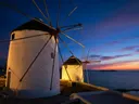 Verlichte witte windmolens op Mykonos bij avondschemering met zee op de achtergrond
