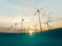 Windturbines op zee bij zonsondergang met oranje en turquoise lucht