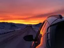Zonsondergang boven een besneeuwde weg, gezien vanuit het raam van een auto